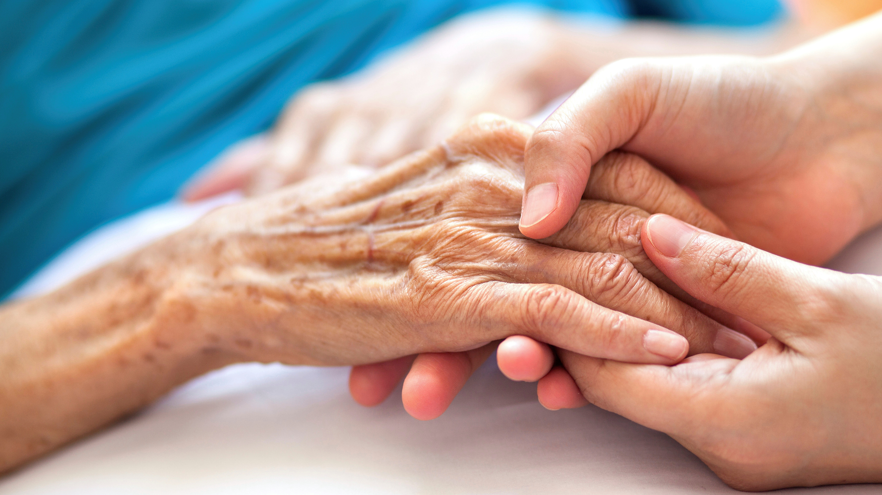 Mladší ruka drží starší, vrásčitou ruku. Symbolizuje soucit, podporu a péči o seniory.