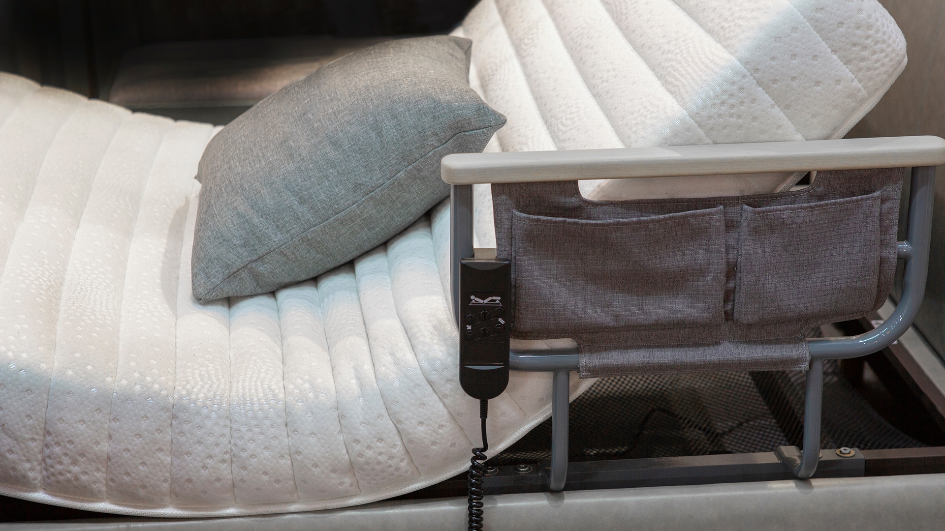 Polohovací postel s dálkovým ovládáním a úložným prostorem. Ilustruje pomůcky pro péči o osoby s omezenou hybností.