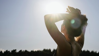 Žena se natahuje k jasnému slunci, symbolizující péči o sebe a hledání světla.