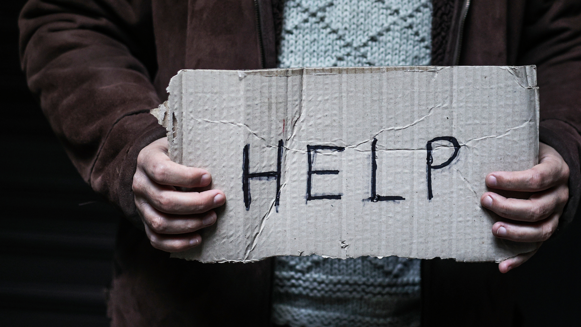 Ruce držící kartonovou ceduli s nápisem "HELP". Symbolizuje volání o pomoc a rizika spojená s domácí péčí.